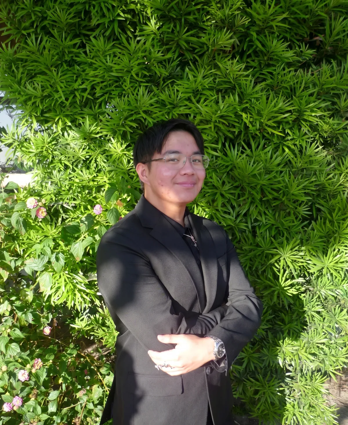 Collin Ong, in a dark suit, standing in front of a hedge