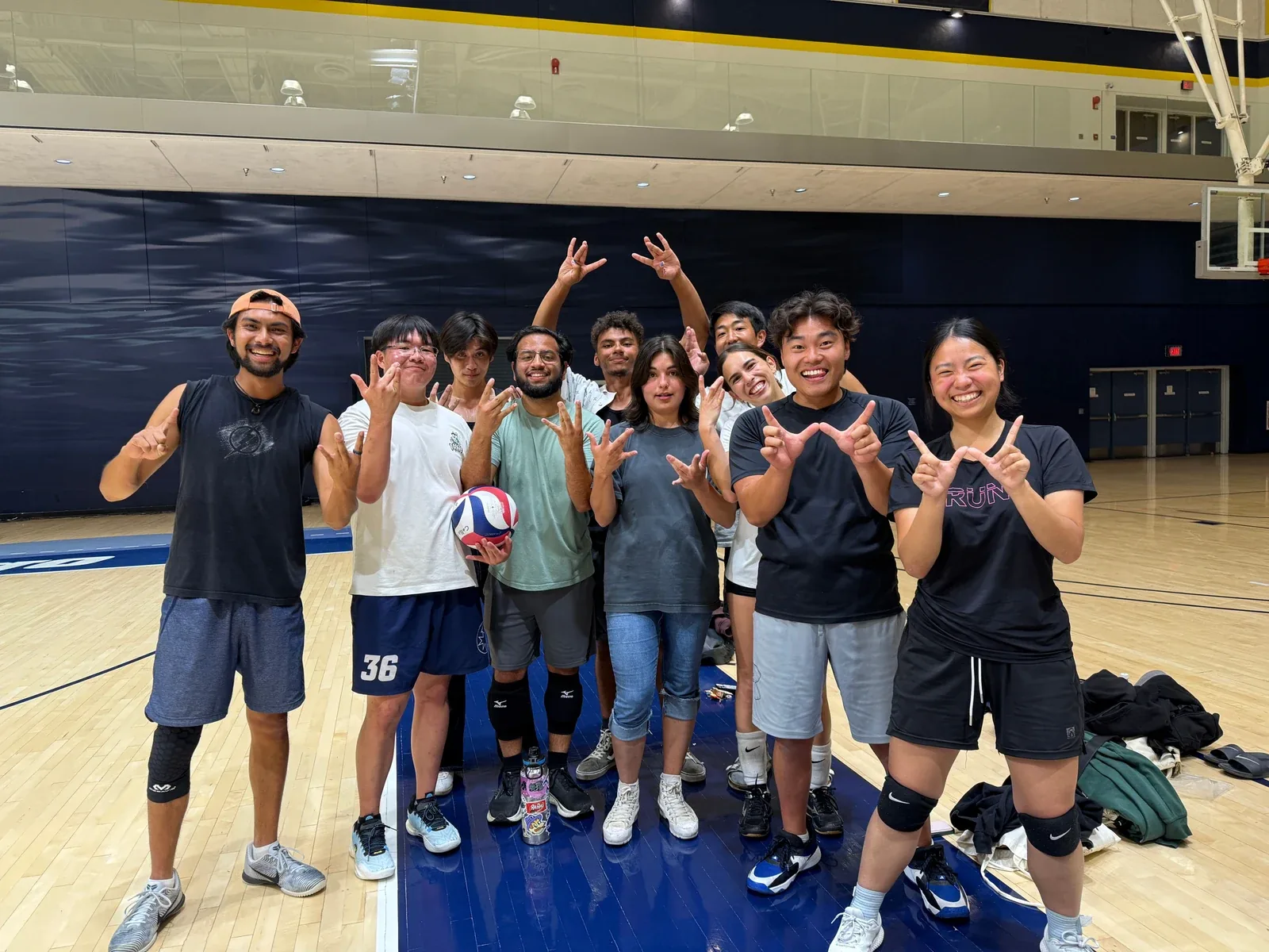 Players posing with a volleyball on an indoor court, arms raised