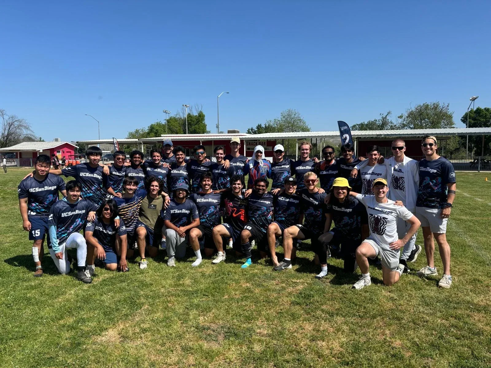 An ultimate frisbee squad in navy jerseys, lined up and kneeling on a grass field
