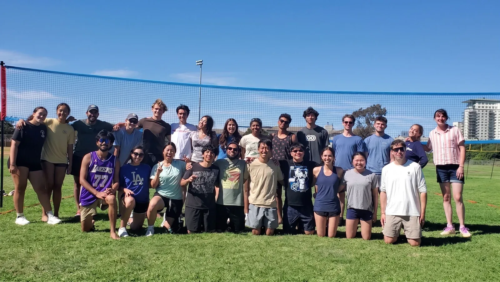 A large group posed in front of an outdoor volleyball net on a clear day